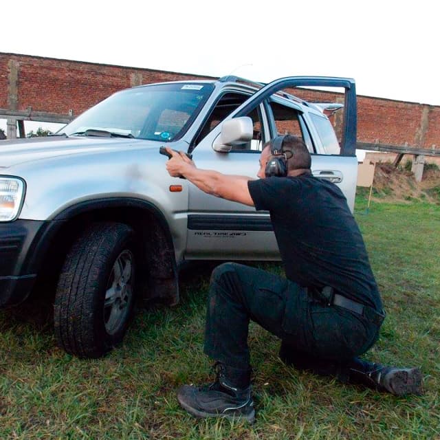 Alumno usando un vehículo como cobertura mientras realiza un ejercicio de tiro defensivo con pistola en un curso avanzado de TDU.